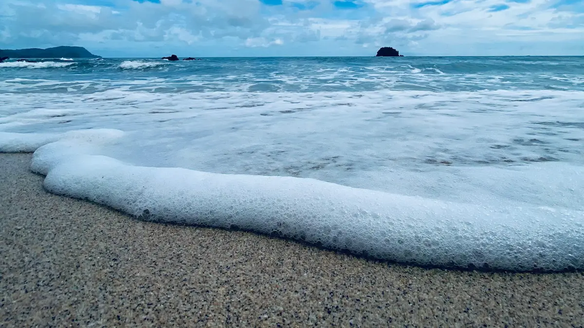 ombak menyapu pasir putih dengan pulau kecil di kejauhan